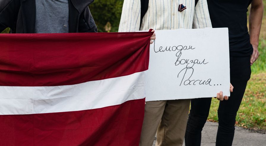 Плакат с надписью "Чемодан вокзал Россия ..." и флаг Латвии. Архивное фото
