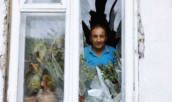 Мужчина смотрит из окна своего дома в Куйбышевском районе Донецка, получившего повреждения в результате обстрела со стороны ВСУ