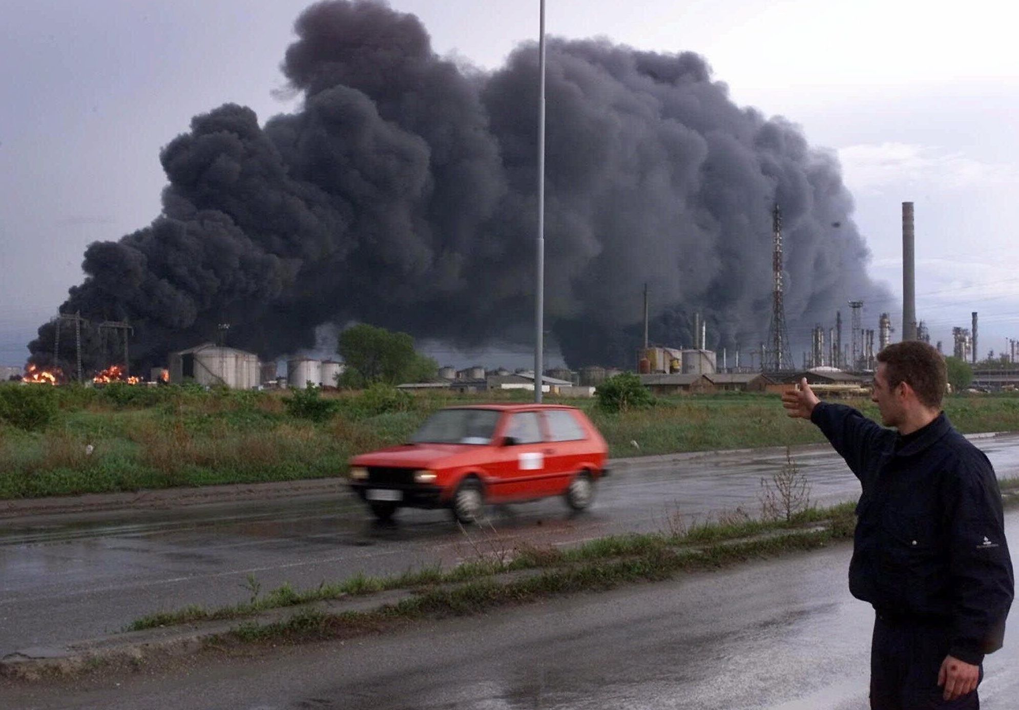 Сотрудник службы безопасности указывает на горящие резервуары нефтеперерабатывающего завода в Панчево после бомбардировки НАТО, 18 апреля 1999 года