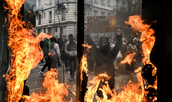 Протестующий держит табличку с надписью "В шоке от сгоревшего пластика, но не от наших украденных пенсий" во время демонстрации 1 мая, Лион, Франция