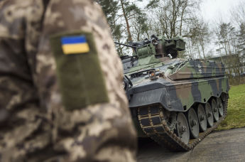Украинский солдат стоит перед БМП