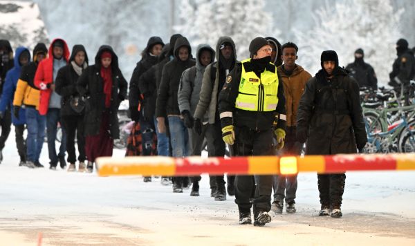 Финский пограничник сопровождает группу мигрантов на международном пограничном переходе в Салле, Финляндия, 23 ноября 2023 года
